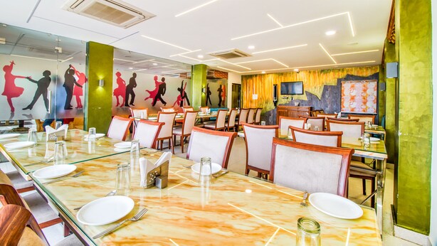 Un espace repas avec des tables et des chaises en verre, et une fresque représentant des danseurs sur le mur.