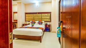 Une chambre d’hôtel avec un grand lit, une tête de lit en bois, une table de chevet et une pancarte indiquant l’emplacement de la salle de bain.