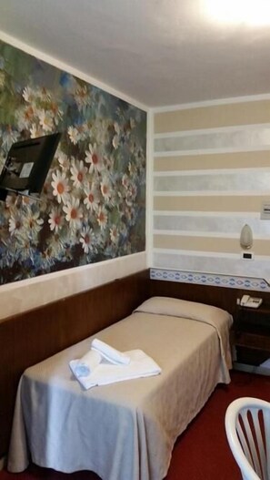 Una habitación de hotel con una cama individual, un escritorio, una silla y un mural floral en la pared.