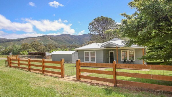 Une maison de plain-pied avec un porche, une cour clôturée et une chaîne de montagnes en arrière-plan.