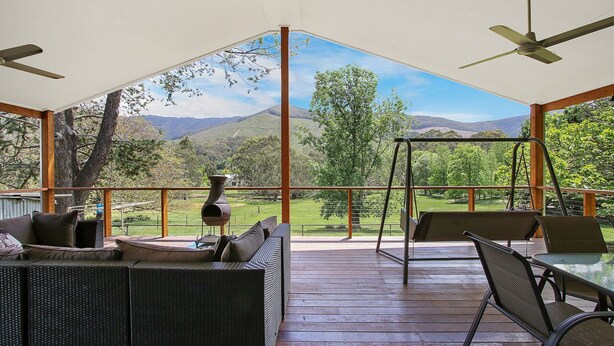 Un espace extérieur abrité, aménagé avec des meubles en osier, une balançoire et offrant une vue sur un paysage montagneux.