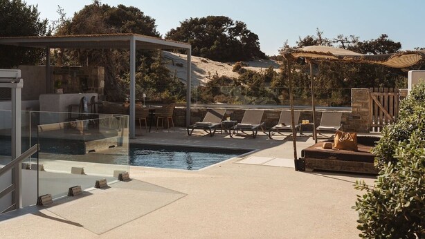 A modern outdoor pool area with glass-enclosed seating, lounge chairs, and a clear view of the surrounding landscape. - Cedar Forest Oceanfront Villa, 4BR Private Pool (Naxos)