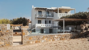 A modern two-story house with a stone wall entrance, a balcony, and a covered outdoor seating area. - Cedar Forest Oceanfront Villa, 4BR Private Pool (Naxos)