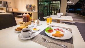 Un desayuno de hotel con una mesa para dos, que incluye tostadas, café, huevos, jamón y salchichas.