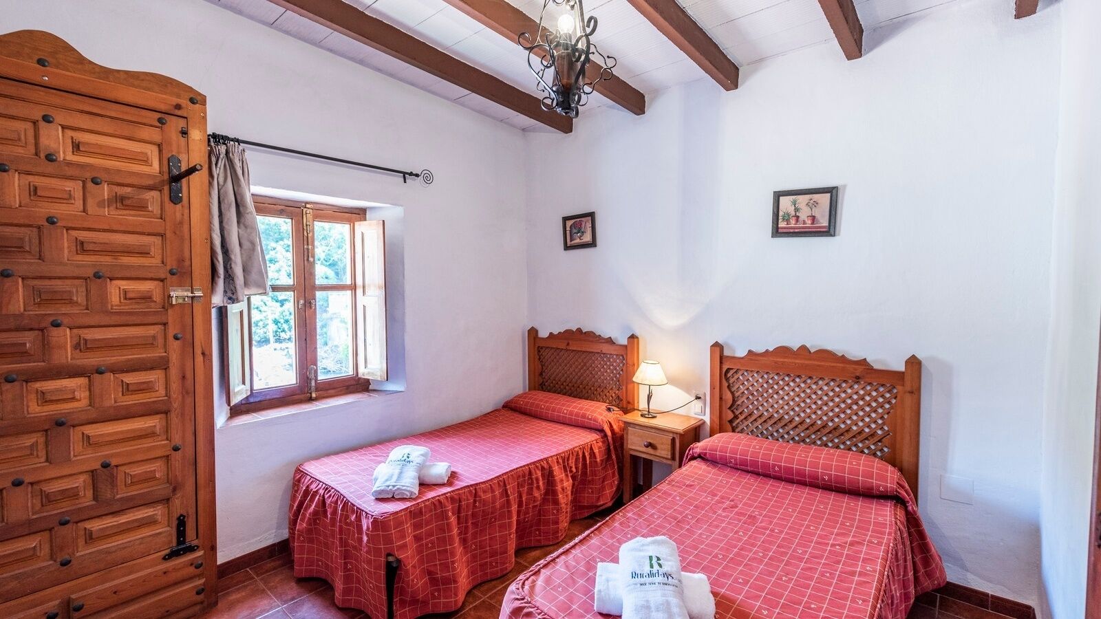 Habitació amb dos llits individuals, un armari de fusta, una finestra amb cortines i un penjallum.