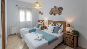 Ein Hotelzimmer mit zwei Betten, einem Holz-Kopfteil, Nachttischlampen, einem Heizkörper und einem Fenster mit Vorhängen.