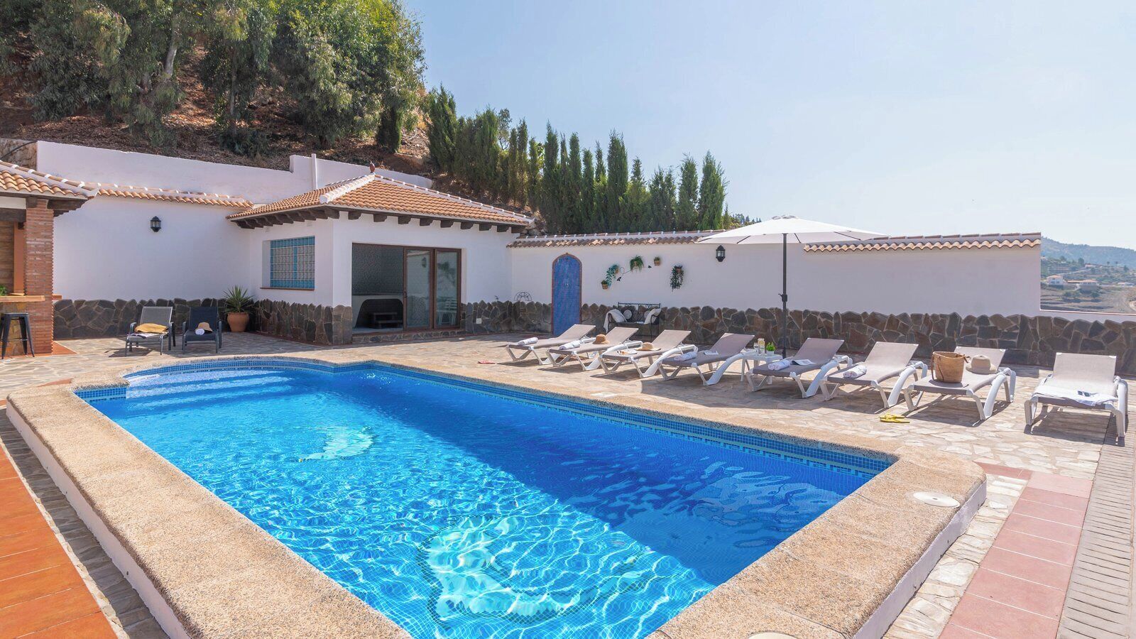 A swimming pool with lounge chairs and a stone wall.