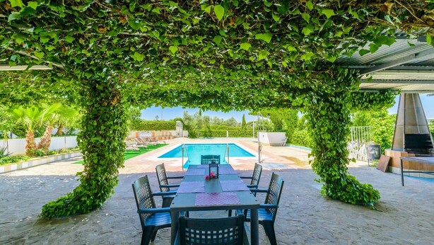 Zona exterior coberta amb piscina, envoltada de vegetació i una taula amb cadires.