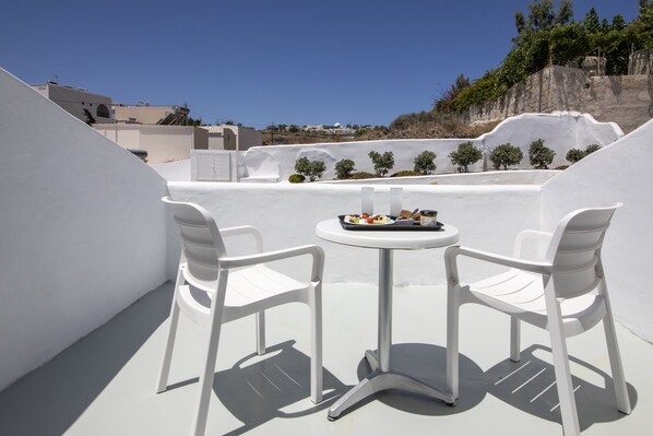 A rooftop terrace with white chairs and a small table, featuring a clear view of the surrounding landscape and buildings.