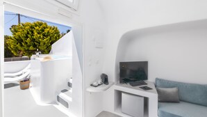 Ein modernes, weißes Interieur mit einer Couch, einem kleinen Schreibtisch mit Computer und einem Fenster mit Blick auf Grünflächen.