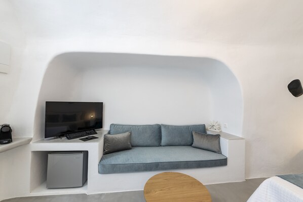 A modern room with a built-in sofa, a flat-screen TV, a small refrigerator, and a wooden coffee table. - Eva's House (Santorini)