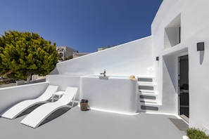 A modern outdoor lounge area with white lounge chairs, a hot tub, and a small table with a bottle and a hat. - Eva's House (Santorini)