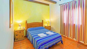 A bedroom with a wooden bed, two bedside tables, a nightstand, a striped curtain, and a wall-mounted lamp. - La Chumbera Órgiva by Ruralidays (Granada)
