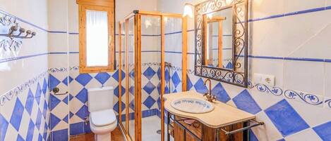 A bathroom with a toilet, shower, and sink, featuring blue and white diamond-patterned tiles.