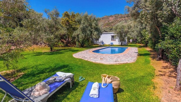 A pool area with lounge chairs, a stone pathway, and a building in the background.