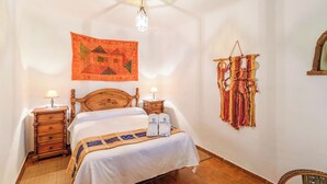 A bedroom with a wooden bed, two bedside tables with lamps, a hanging tapestry, and a macrame wall hanging.