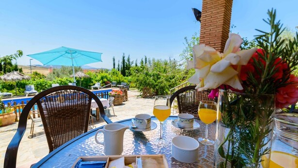 An outdoor dining area with wicker chairs, a table with a pitcher, cups, and glasses, and a blue umbrella. - El Torcal Antequera - La Higuera by Ruralidays (Málaga)