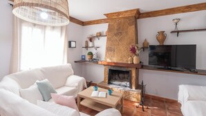 A living room with a stone fireplace, a television, and a wicker ceiling light. - El Torcal Antequera - La Higuera by Ruralidays (Málaga)