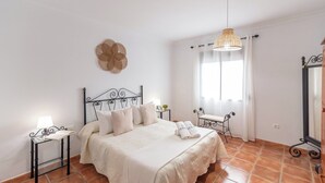 A bedroom with a bed, bedside tables, a chair, a window with curtains, and a hanging light fixture. - El Torcal Antequera - La Higuera by Ruralidays (Málaga)
