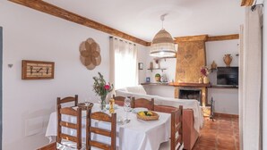 A dining area with a table set for two, wooden chairs, a hanging light fixture, and a stone fireplace in the background. - El Torcal Antequera - La Higuera by Ruralidays (Málaga)