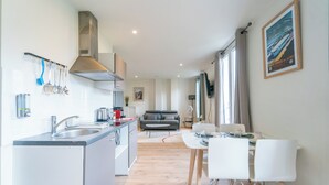 Una cucina moderna con piano cottura integrato, una zona pranzo con sedie bianche e un soggiorno con divano.
