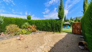 A garden with a stone pathway, various plants, a wooden gate, and a pool in the background.