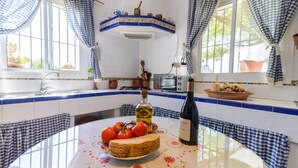 A kitchen with a round table, a bottle of wine, and a plate of tomatoes and bread.