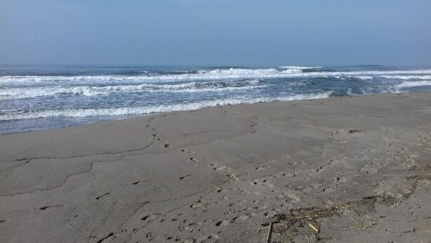 A beach with footprints in the sand and waves crashing onto the shore.