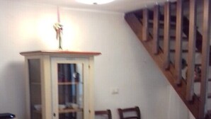A dining area with a wooden table and chairs, a cabinet with glass doors, and a staircase in the background.
