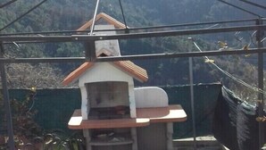 A small outdoor grill structure with a chimney, surrounded by a metal frame and supported by ropes.