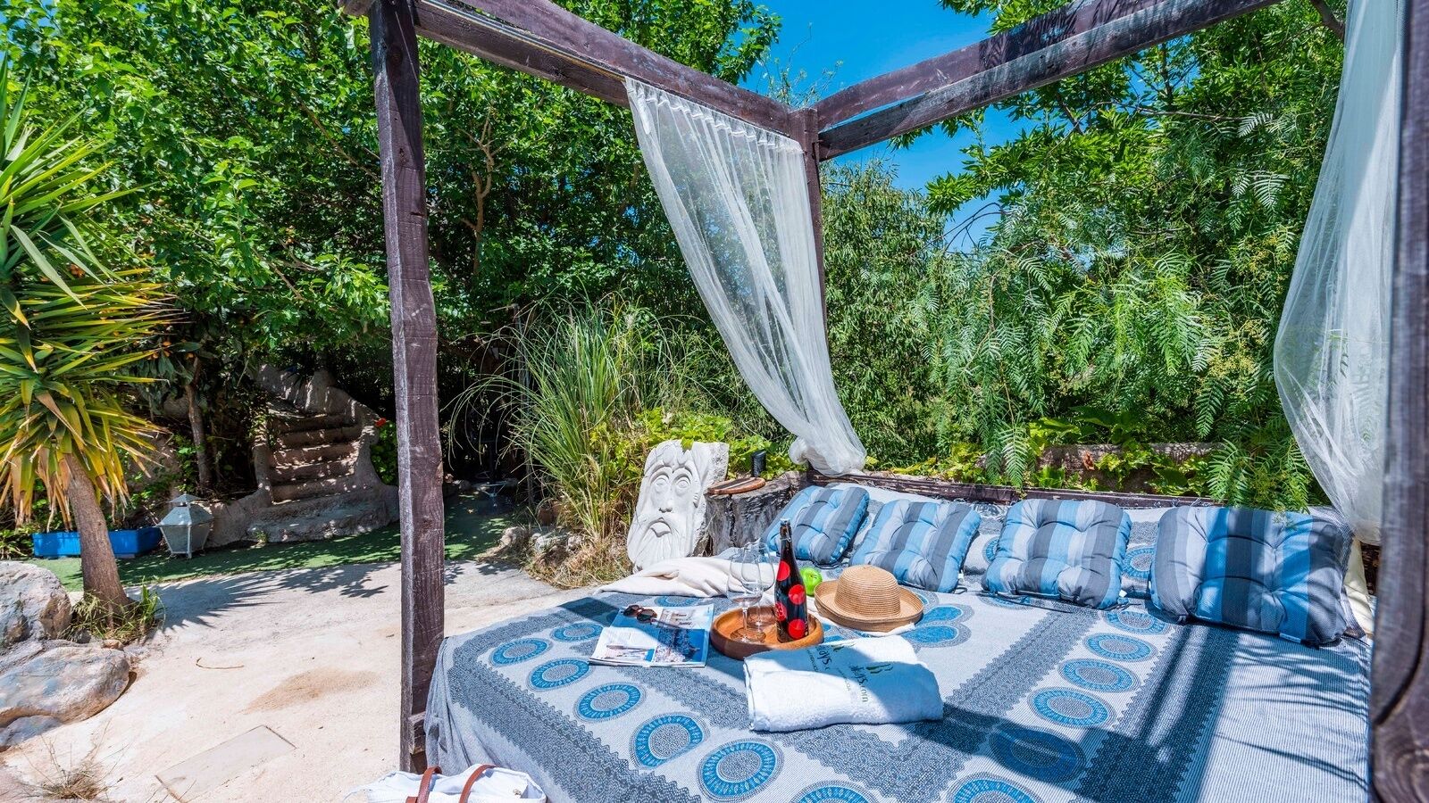 A covered outdoor seating area with a patterned tablecloth, cushions, and a bottle of wine.