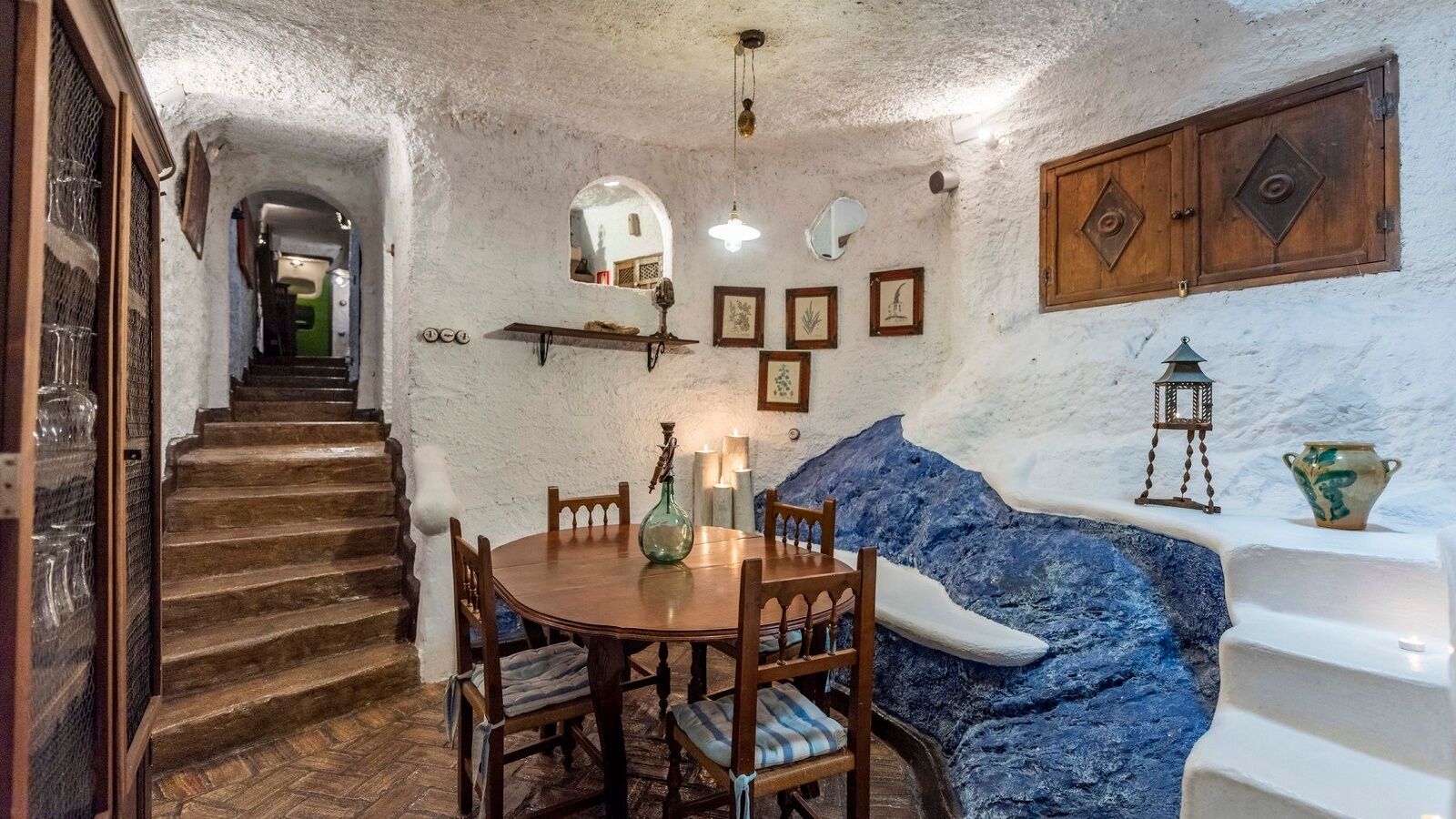 A dining area with a wooden table and chairs, a blue textured wall, and a staircase leading to another room.