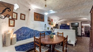 Interior acolhedor e rústico com mesa de madeira redonda, assentos estofados em azul e parede de pedra.