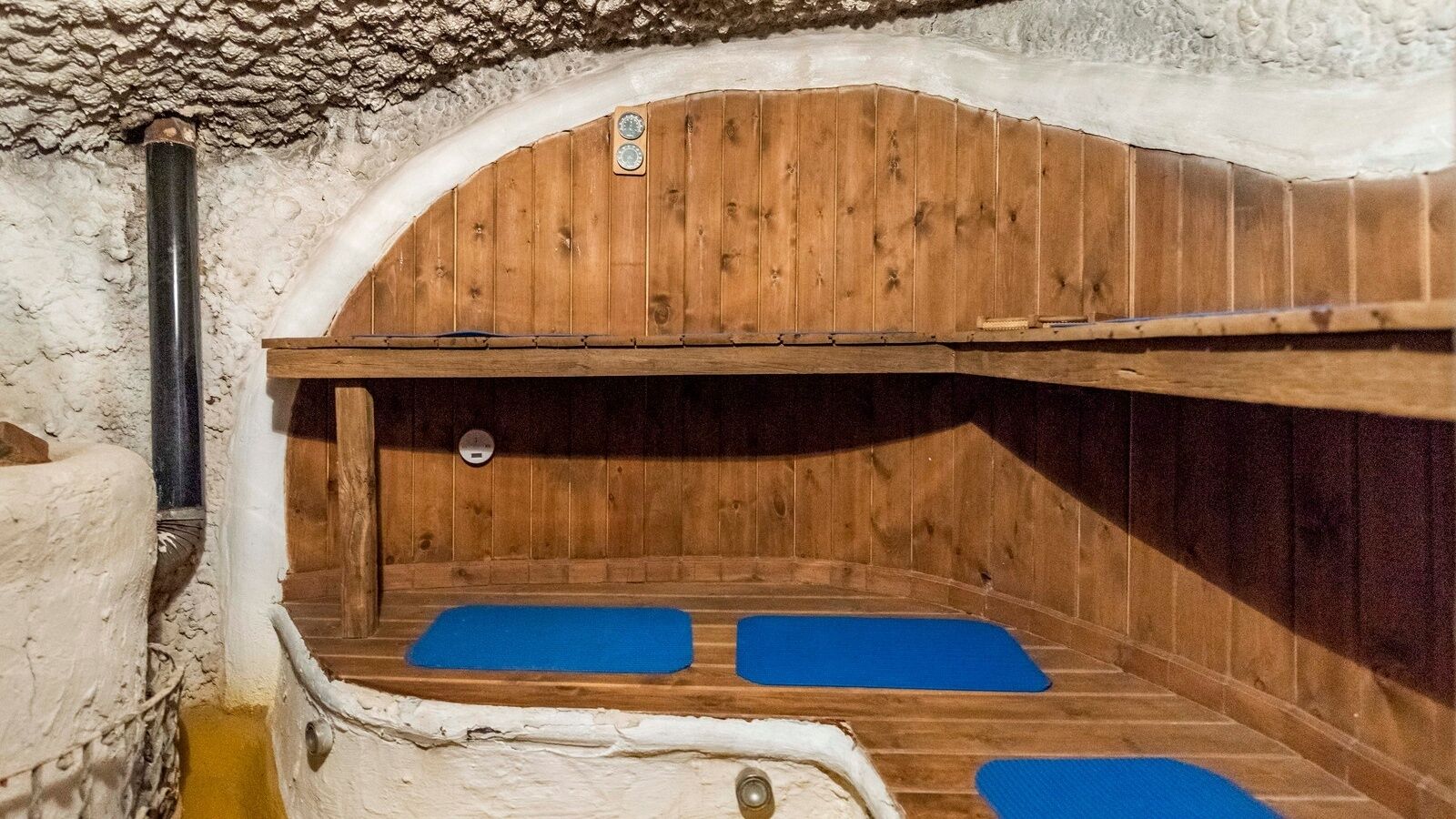 Una sauna de madera con dos alfombras azules, un banco de madera y una pared de piedra.