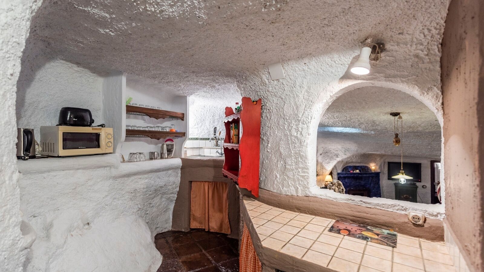 A cozy, rustic kitchen with a microwave, shelves, and a red cabinet.