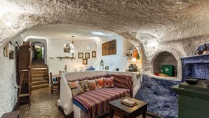 Um espaço habitável subterrâneo com sofá, mesa e escada que dá acesso a outra área.