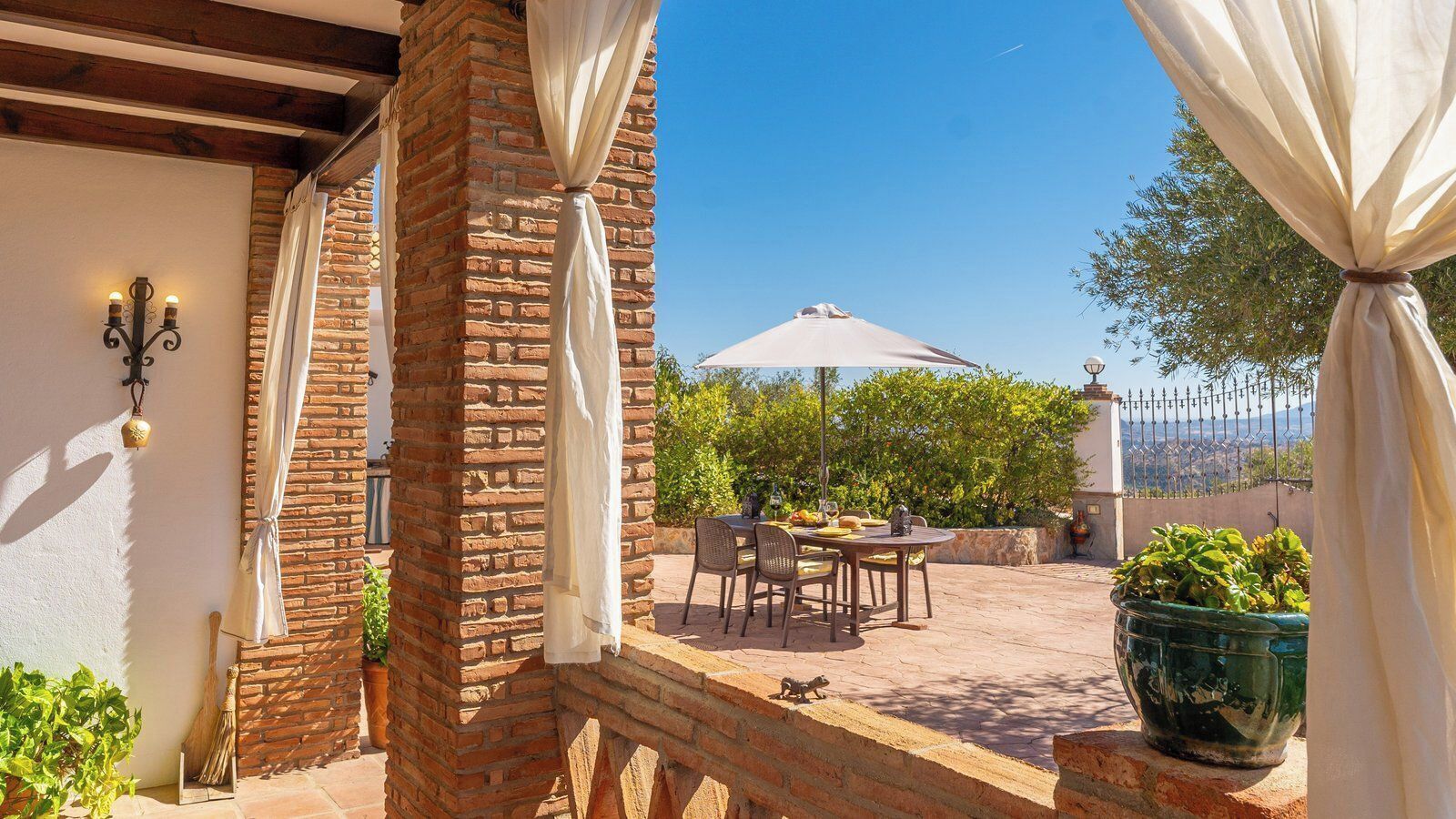 Une terrasse extérieure avec un mur en briques, une table avec des chaises et un grand parasol.