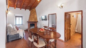 Zona de menjador acollidora amb una llar de pedra, taula de fusta i cadirees.