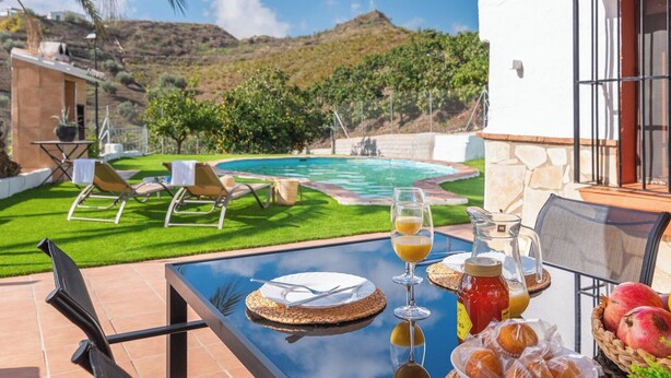 Un pati amb taula preparat per esmorzar, amb vista a una piscina i un jardí exuberant.