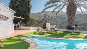 Zona de piscina amb vistes a les colines, un edifici blanc i mobles d'exterior.