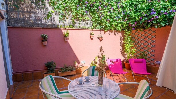 A patio with a round table and chairs, potted plants, and a lattice wall. - Zulaikhah Suite Ronda by Ruralidays (Málaga)