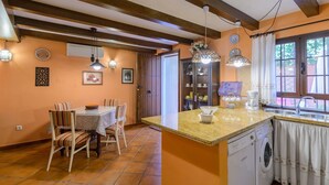 A kitchen with a dining area, featuring a tiled floor, wooden beams, a washing machine, and a sink. - Zulaikhah Suite Ronda by Ruralidays (Málaga)