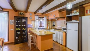 A kitchen with a central island, wooden beams on the ceiling, and a refrigerator on the right. - Zulaikhah Suite Ronda by Ruralidays (Málaga)