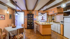 A cozy kitchen with a dining area, featuring a tiled floor, wooden beams, and a central island with a sink and a refrigerator. - Zulaikhah Suite Ronda by Ruralidays (Málaga)
