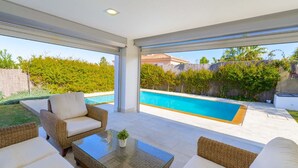 Un espace de vie extérieur moderne, doté d'une piscine, de meubles en osier et d'une table en verre.