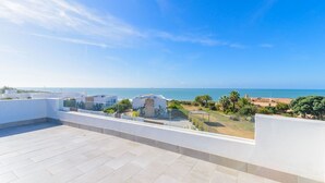 Une terrasse sur le toit offrant une vue sur la mer, des bâtiments blancs et quelques espaces verts.