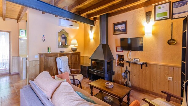 A cozy living room with a sofa, a wooden table, a fireplace, and a TV mounted on the wall.