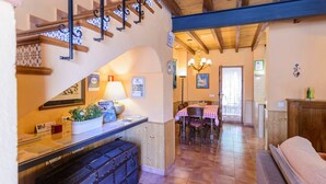 A cozy interior with a wooden staircase, a reception desk, a dining area with a checkered tablecloth, and a hallway leading to a kitchen.
