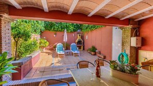 An outdoor patio with a brick wall, a grill, and seating area with chairs and tables.