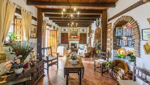 A cozy dining area with a long wooden table, chairs, and a chandelier. There are bookshelves and a fireplace in the background. - Las Monjas - Atroe Periana by Ruralidays (Málaga)